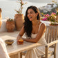 Smiling woman wearing an exquisite Wexari gold-toned sculptural liquid metal collar necklace and matching abstract teardrop earrings on an elegant outdoor terrace.
