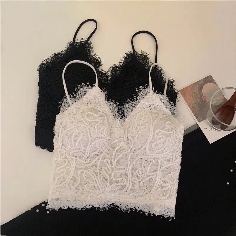 White and black Zyrin lace cropped camisoles laid flat, showcasing the delicate floral lace, eyelash trim V-neck, and slim spaghetti straps.