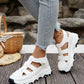 White Kryzen chunky platform sandals with cut-out straps, worn by a model in jeans with a straw hat and basket on a wooden deck.