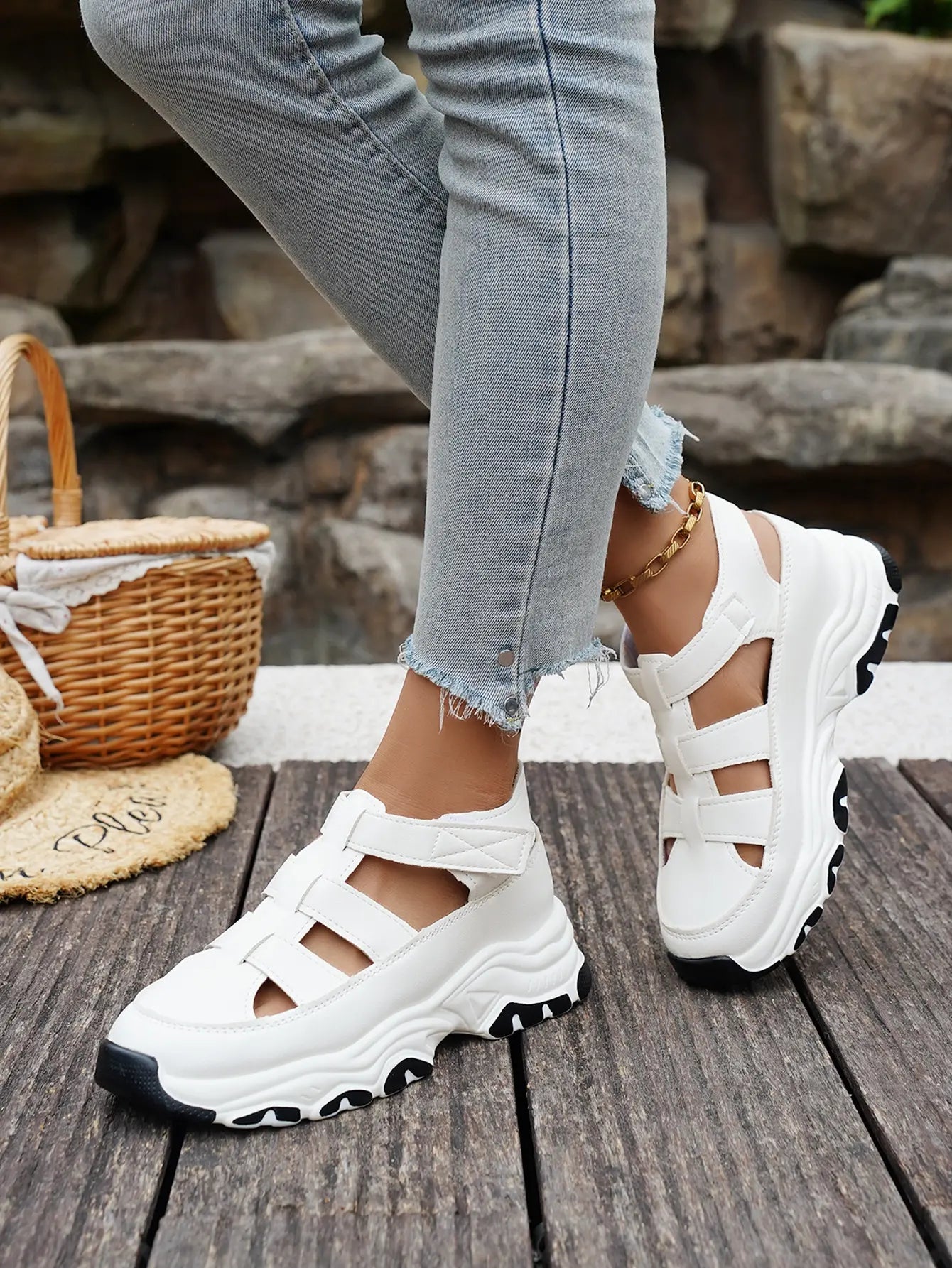 White Kryzen chunky platform sandals with cut-out straps, worn by a model in jeans with a straw hat and basket on a wooden deck.