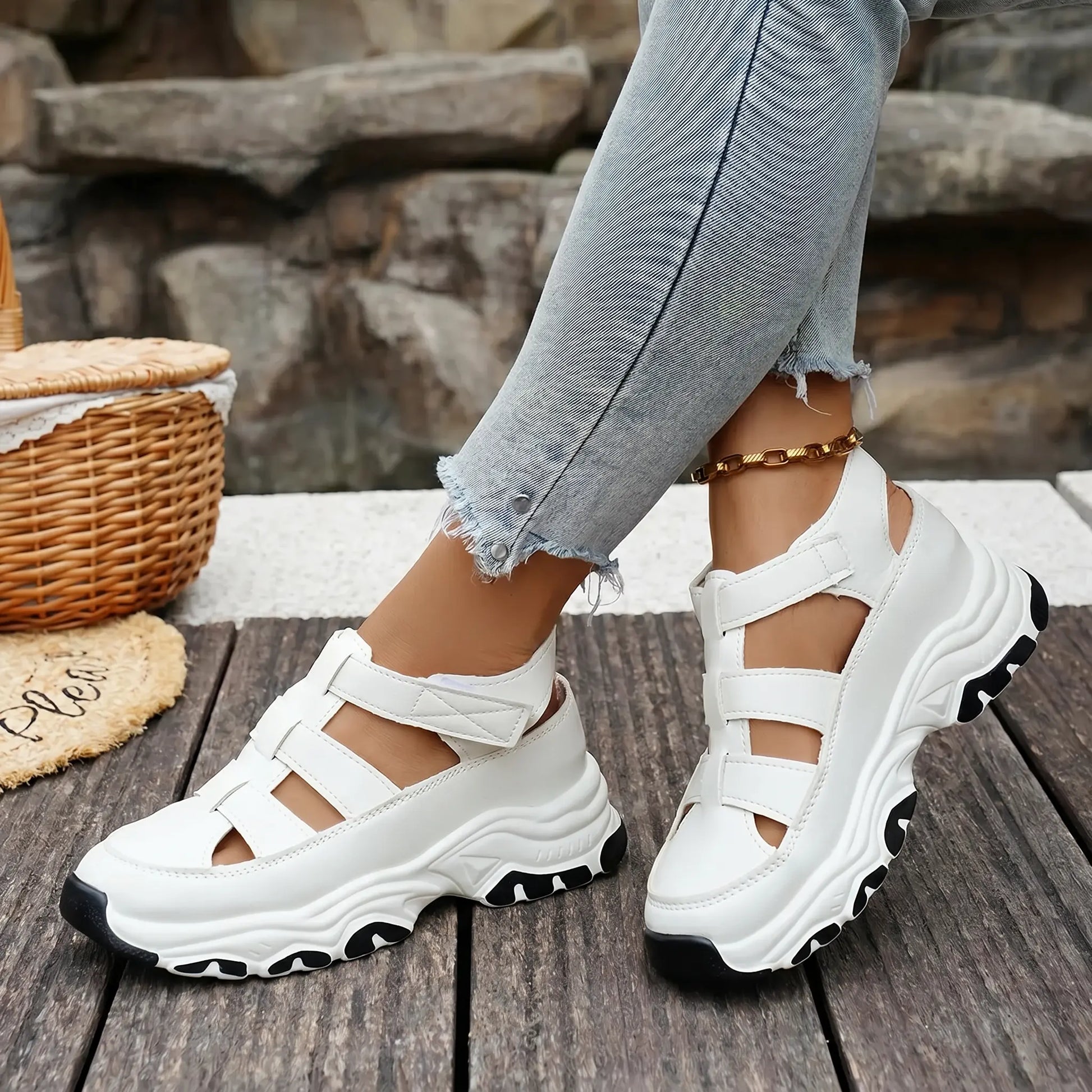 A woman wearing white Kzyzen sporty chic chunky platform sandals with open-back cut-out straps and hook-and-loop closure, styled with distressed denim jeans against a natural wood plank background.
