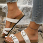 Lifestyle image of white Lyraea cork footbed slide sandals worn with distressed denim jeans, featuring dual adjustable straps with antique brass buckles and a contoured cork footbed.