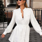 Woman wearing a white cotton linen mini dress with lantern sleeves, ruffled placket, and pom-pom hem, standing outdoors on a city street.