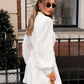 Woman from the back-left wearing a white cotton linen mini dress with lantern sleeves, ruffled placket, pom-pom hem, and a self-tie belt, styled for a romantic bohemian look outdoors.