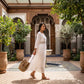 Woman in a white Kivren bohemian embroidered linen midi dress, featuring a notched V-neck and three-quarter sleeves, walking through a beautiful riad courtyard.