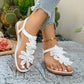Women's white flat thong sandals adorned with layered fabric floral appliqués and featuring an elasticated slingback strap, styled with distressed denim jeans in an outdoor setting.