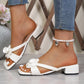 Elegant white heeled mules adorned with delicate floral rose embellishments, featuring a square open-toe design and a comfortable block heel, shown on a model's feet in a lifestyle setting.