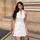 Woman wearing a white sleeveless linen-blend A-line mini dress with a halter neckline and button-front detail, standing outdoors against a stone building.