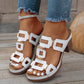 Women's white heeled slide sandals with geometric gold-tone hardware and a chunky block heel, styled with distressed denim and an anklet on a wooden deck.