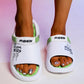 White Kaelos comfort slides with lime green accents worn on feet, featuring embossed 'FASHION' and 'LIFE IS BEAUTIFUL' text on the straps and side.