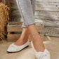 Elegant white pointed-toe knit flats for women, featuring a chic bow detail and subtle metallic sheen, worn with denim jeans.
