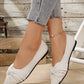 White knit pointed-toe flats adorned with a delicate bow detail, shown on a model's feet paired with denim jeans, offering a chic and comfortable look.