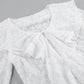 Close-up of an elegant white lace blouse showcasing intricate floral patterns, a ruffled cascading front detail, and a V-neckline. The sheer fabric texture is clearly visible.