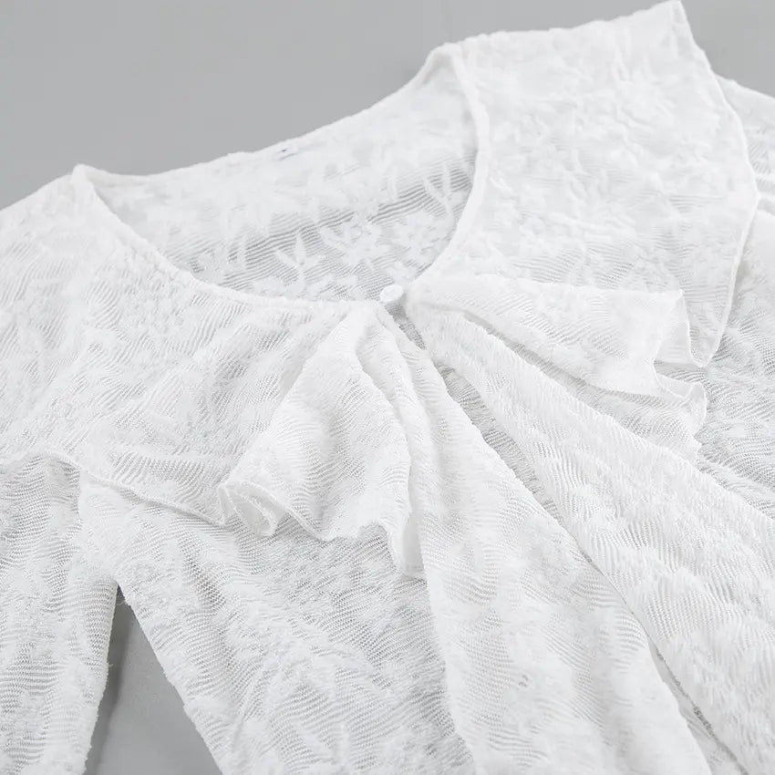 Close-up of an elegant white lace blouse showcasing intricate floral patterns, a ruffled cascading front detail, and a V-neckline. The sheer fabric texture is clearly visible.