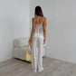 Woman wearing a white lace camisole and matching wide-leg pants, holding a yellow handbag, shown from the back in a minimalist studio setting.