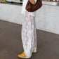 White floor-length A-line lace maxi skirt styled with a white t-shirt, brown bag, and yellow sneakers. The sheer lace allows visibility of the legs.
