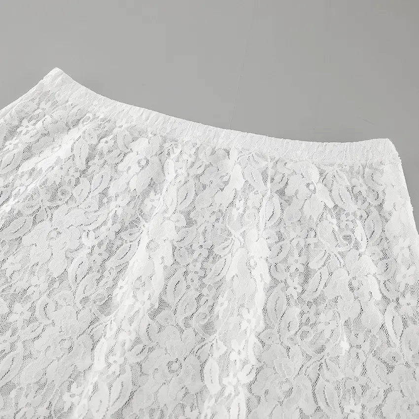 Close-up of a high-waisted white lace maxi skirt, showcasing the intricate floral lace pattern and the integrated waistband. The fabric is sheer and matte, with a delicate texture.