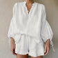 White linen-blend two-piece set featuring a loose V-neck blouse with voluminous lantern sleeves and ruffled hem shorts worn by a woman, showcasing elegant bohemian summer style.