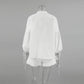 Back view of a white linen-blend set featuring a loose blouse with voluminous lantern sleeves and adjustable tie cuffs, paired with shorts that have a delicate ruffled hem. This ensemble showcases bohemian chic.
