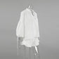 White linen blend two-piece set featuring a V-neck blouse with voluminous lantern sleeves and adjustable tie cuffs, paired with high-waisted shorts with a ruffled hem, shown from the side.