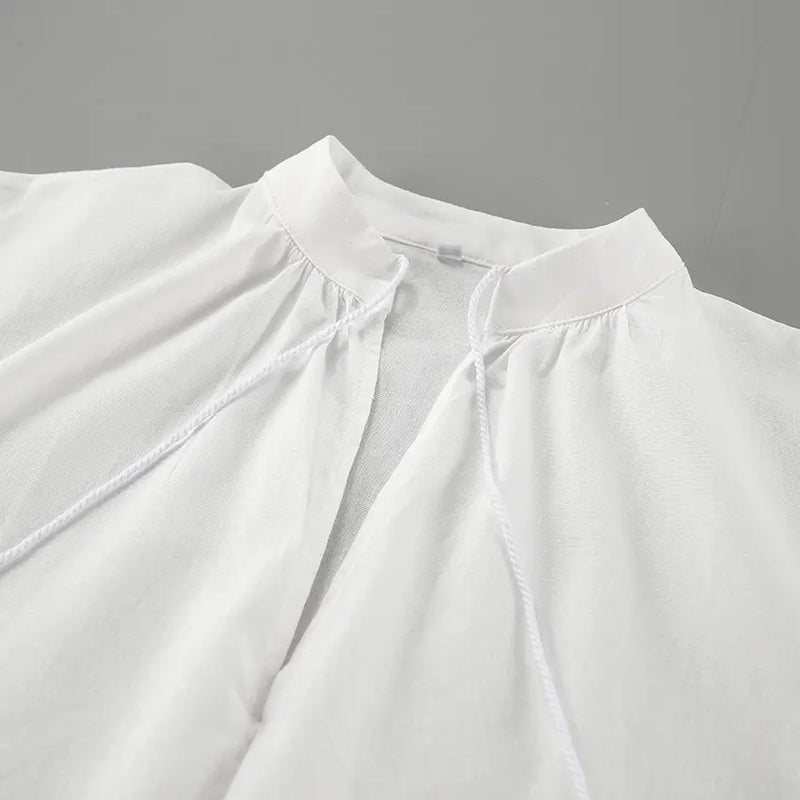 Close-up view of a white linen blend top's V-neckline featuring delicate drawstring ties and gathered fabric details.