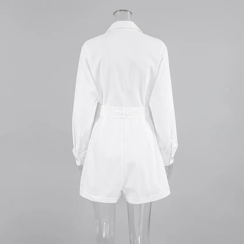 Back view of a white long-sleeved collared playsuit featuring a belted waist and tailored short bottoms, presented on a studio grey background.