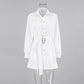 Elegant white long-sleeve playsuit with a collared neckline, belted waist featuring a gold buckle, and tailored shorts, presented front-on in a studio setting.