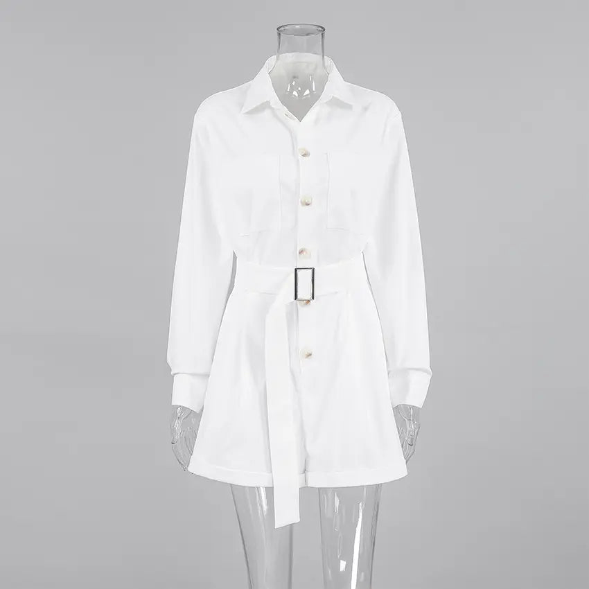 Elegant white long-sleeve playsuit with a collared neckline, belted waist featuring a gold buckle, and tailored shorts, presented front-on in a studio setting.