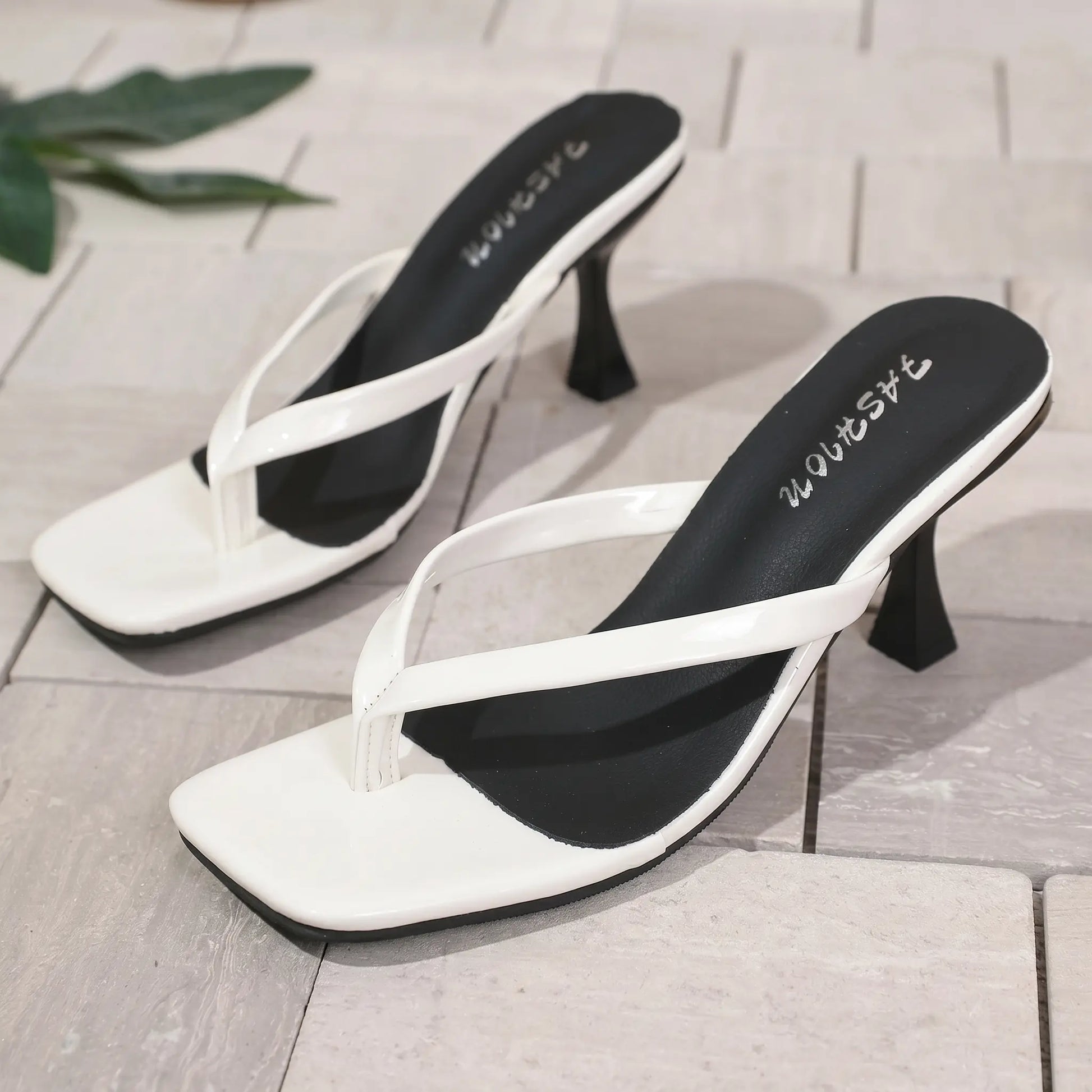 White patent heeled flip-flops with a square toe and delicate thong strap, featuring a sculptural stiletto heel and a black insole with subtle white 'FASHION' lettering.
