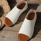 Pair of white perforated PU leather women's flat sandals with a peep-toe and tan lining, styled on a rustic wooden surface next to a straw hat.