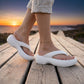 Person walking on a wooden boardwalk, wearing Mivon Pristine White elevated platform thong sandals with a chunky EVA sole and wide V-strap, at sunset over the ocean.