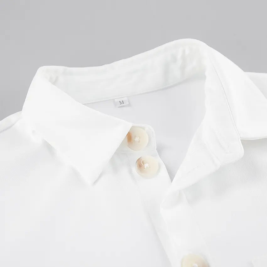 Close-up of a white collared playsuit featuring pearlescent button details and a subtle 'M' size tag.
