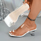 Elegant white square-toe mule sandals with clear PVC straps adorned with sparkling rhinestones, shown on a woman's foot with a clear block heel and a subtle toe ring.