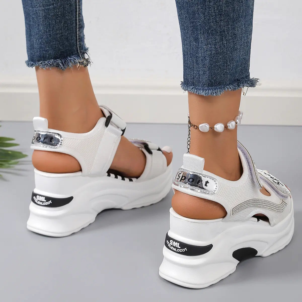 White sporty platform sandals adorned with shimmering rhinestones, featuring adjustable hook-and-loop straps and a chunky sole, shown on feet with denim.