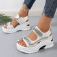 White embellished platform sandals with 'Sport' text on the straps, shown on a woman's feet with ripped jeans and a pearl anklet, offering a sporty chic summer look.