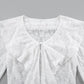 Close-up view of a white, sheer floral lace blouse showcasing a V-neckline, a dramatic cascading ruffle front, and intricate fabric texture.