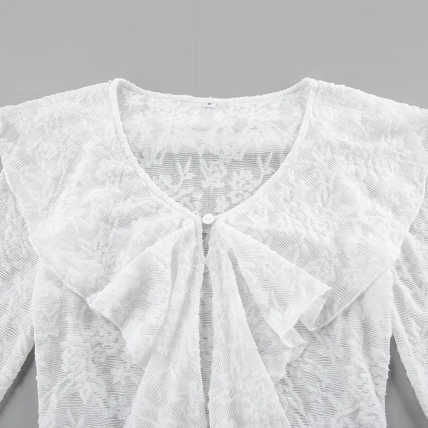 Close-up view of a white, sheer floral lace blouse showcasing a V-neckline, a dramatic cascading ruffle front, and intricate fabric texture.