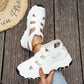 White sporty chic chunky platform sandals with open-back and cut-out straps, styled on feet with denim jeans and a straw hat, set against a wooden background.