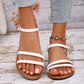 White vegan leather strappy flat sandals with delicate three vamp straps and an adjustable ankle buckle, worn on feet with denim jeans and a turquoise ankle bracelet.