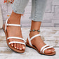 White strappy flat sandals worn by a woman, featuring three thin vamp straps and an adjustable ankle buckle with antique gold finish. Shown from a three-quarter angle with a hint of denim jeans and a boho-style anklet.