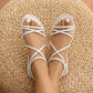 White bohemian strappy flat sandals worn on feet, featuring thin crossover tubular straps and a gathered elastic heel band, seen from a top-down view on a woven mat.