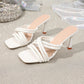 White strappy heeled square toe mules featuring glossy PU crisscross straps and a flared sculptural heel, displayed on a sparkly textured surface with draped fabric. Includes embossed 'FASHION' text on the insole.