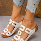 Close-up of a woman's feet wearing white textured slide platform sandals with gold-tone hardware and a cherry charm anklet, styled with distressed denim jeans.