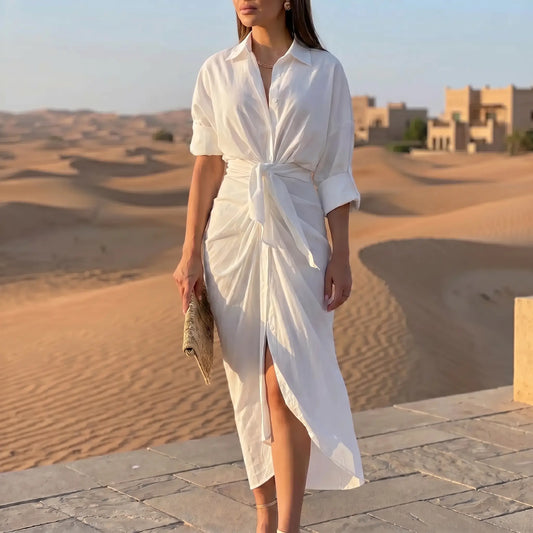 Elegant white tie-waist midi shirt dress with a collared neckline, rolled sleeves, and draped tulip skirt, worn by a model in a sunlit desert scene.