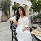 Elegant white tie-waist midi shirt dress with rolled sleeves, worn by a model relaxing at an outdoor cafe. The dress features a pointed collar and a flowing tulip skirt.