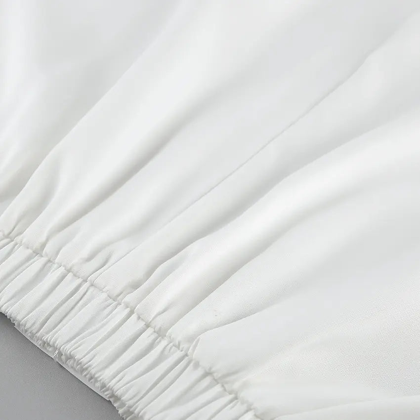 Close-up of the crisp white fabric and elastic waistband of an elegant two-piece set, showcasing the smooth matte texture and refined craftsmanship.
