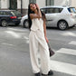 Woman models a chic white sleeveless vest and wide-leg trousers suit ensemble on an urban street, showcasing a modern, elegant look.