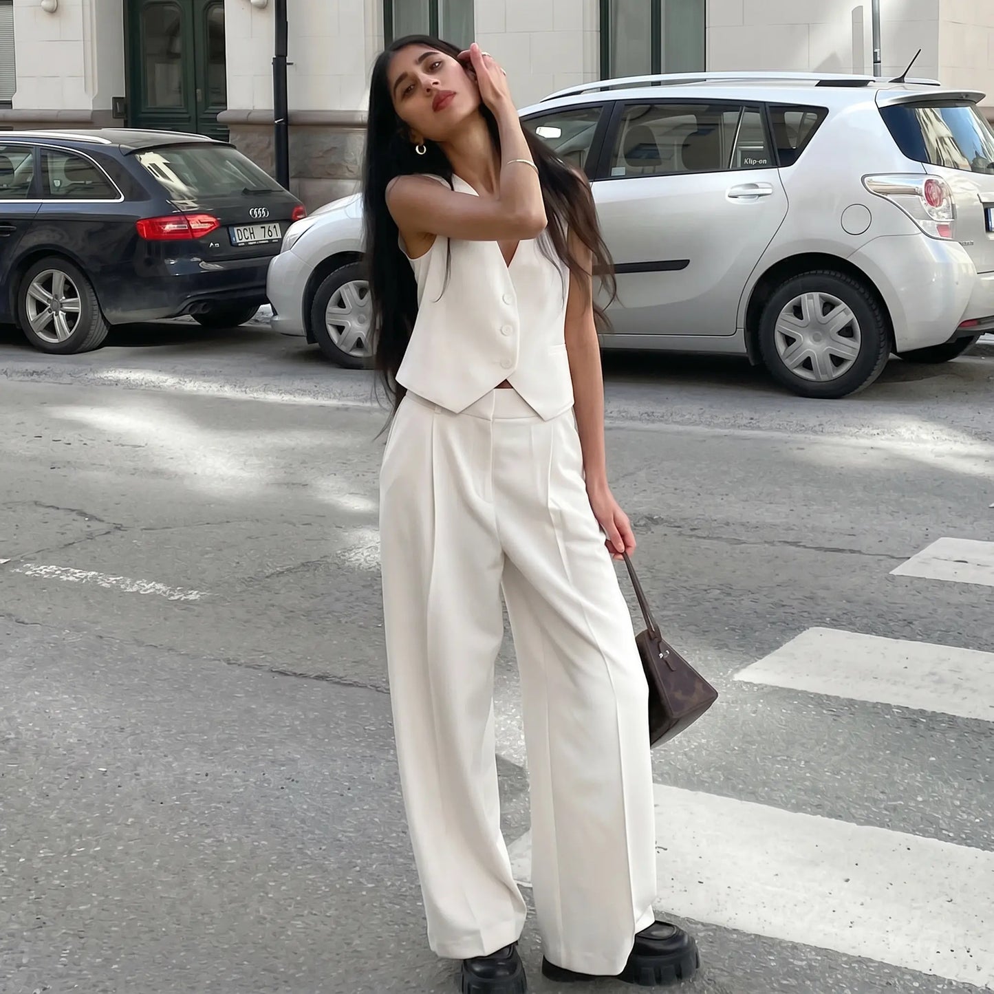 Woman models a chic white sleeveless vest and wide-leg trousers suit ensemble on an urban street, showcasing a modern, elegant look.