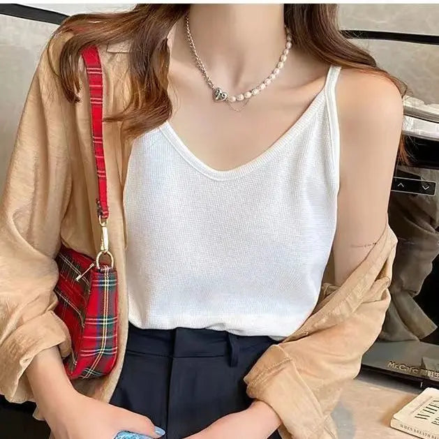Crisp white Koryx waffle knit camisole featuring thin spaghetti straps and a V-neck, worn by a model in a relaxed lifestyle setting. The top highlights its distinctive texture.