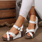Women's white faux leather wedge sandals with criss-cross straps and gold stud details, worn with ripped white jeans and a colorful anklet on a wooden floor.